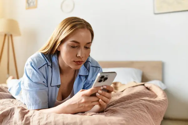 Молодая женщина расслабляется на кровати, занимаясь со своим смартфоном, наслаждаясь уютной ночью. — стоковое фото