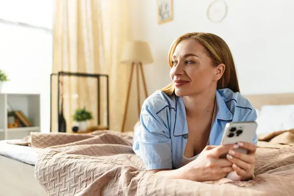 A young and beautiful woman relaxes at home, gazing thoughtfully while holding her smartphone. — Stock Photo