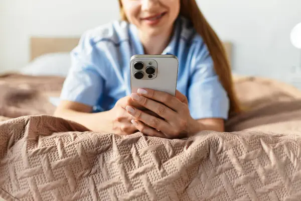 A young woman relaxes on her bed, joyfully using her smartphone in a cozy home. — Stock Photo