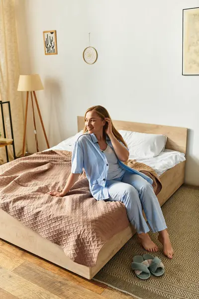 A beautiful young woman sits on the edge of her bed, radiating joy and relaxation in a cozy bedroom. — Stock Photo