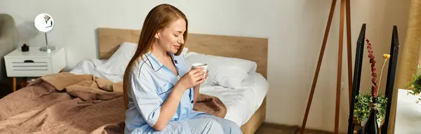 Una giovane donna gode di una bevanda calda mentre è seduta sul suo letto, persa nel pensiero pacifico. — Foto stock