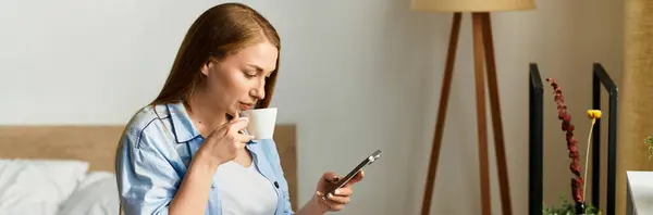 Young woman enjoys tea while browsing her smartphone in a warm home atmosphere. — Stock Photo