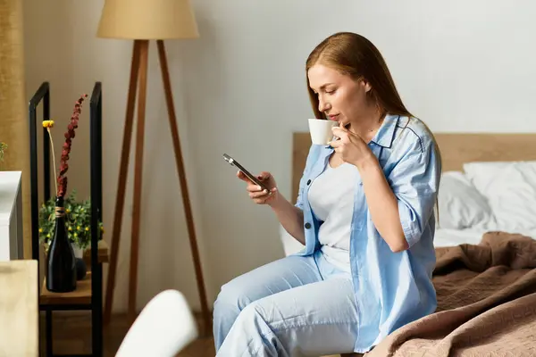 A young woman relaxes at home, sipping tea while scrolling on her phone in a cozy environment. — Stock Photo