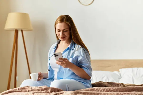 Una giovane donna si gode la mattina in uno spazio confortevole, sorseggiando un drink mentre utilizza il suo smartphone. — Foto stock