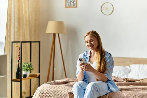 Una hermosa joven relajada en su acogedora casa, sonriendo mientras se conecta con su teléfono cómodamente. - foto de stock
