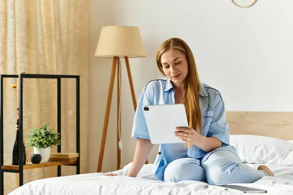 Young woman sits comfortably in cozy bedroom, engaged with her tablet in a serene moment. — Stock Photo