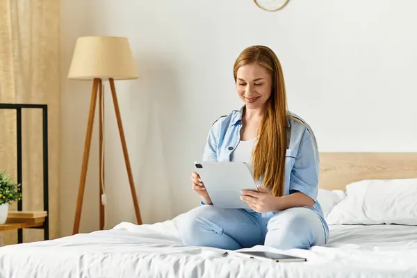 A young woman smiles while using her tablet, seated comfortably on the bed. — Stock Photo