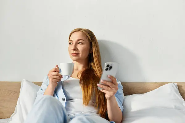 Una giovane donna si rilassa a casa, sorseggiando un drink caldo e usando il telefono in pace. — Foto stock
