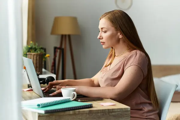 A young woman sits at her desk, focused on her tasks while enjoying home comforts. — Stock Photo