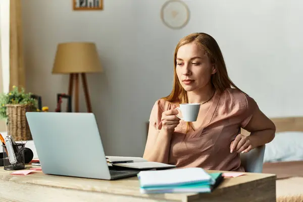 Giovane donna si rilassa nella sua casa accogliente, sorseggiando una bevanda calda e concentrandosi sul suo lavoro. — Foto stock