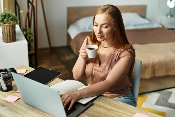 In a warm home atmosphere, a beautiful young woman savors coffee while focusing on her laptop. — Stock Photo