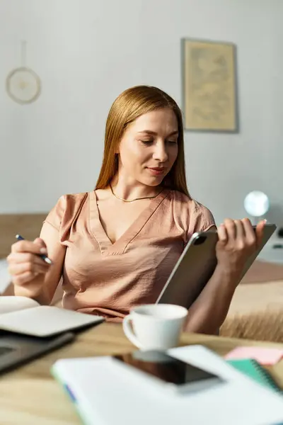 Una donna si rilassa nel suo accogliente spazio di lavoro a casa, annotando note sul suo tablet. — Foto stock