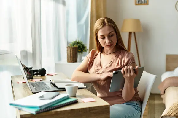 In a comfortable home setting, a young woman engages with her tablet, surrounded by work materials. — Stock Photo