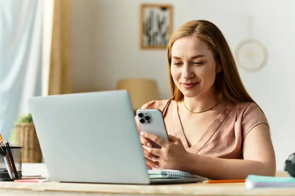 Donna si rilassa a casa, felicemente utilizzando il suo smartphone mentre seduto su una scrivania ordinata. — Foto stock
