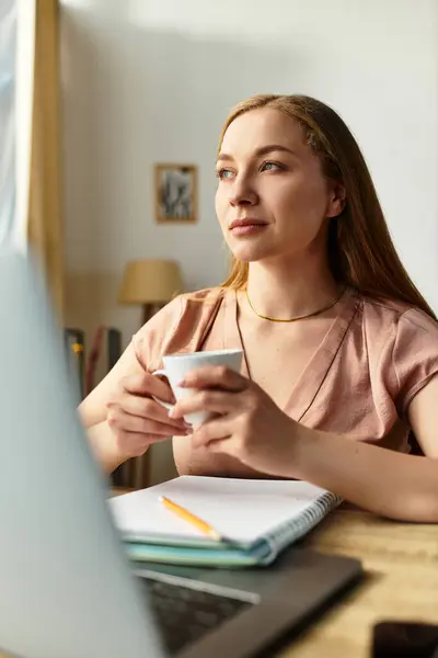 Rilassandosi a casa, una bella giovane donna si siede a un tavolo, sorseggiando un caffè e contemplando. — Foto stock