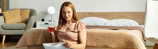 A young woman with long hair savors a cup of tea while reading a book in a cozy space. — Stock Photo