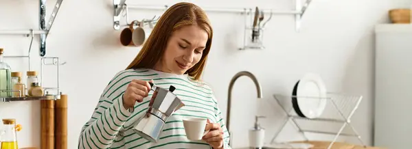 A beautiful woman with long hair pours coffee into a cup, smiling in her inviting kitchen. — Stock Photo