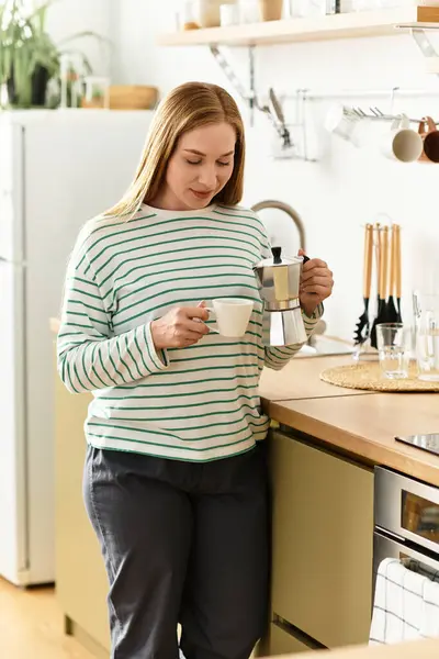 Una giovane donna nella sua accogliente cucina versa caffè fresco, irradiando calore. — Foto stock