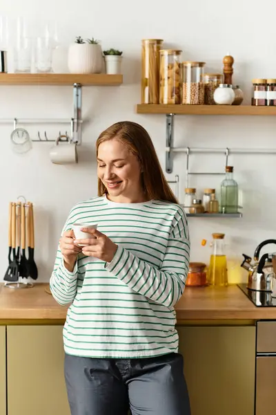 A beautiful young woman smiles as she enjoys a warm beverage, embracing the comforts of home. — стоковое фото