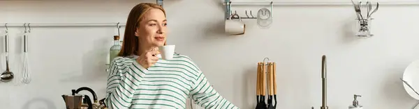 Young woman sips a warm drink while relaxing in her cozy kitchen, radiating comfort and joy. — Stock Photo