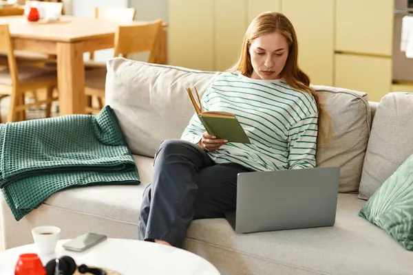 Young woman enjoys her time at home, reading a book while seated comfortably on a couch. — Stock Photo