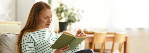 Молодая женщина расслабляется на диване, читая книгу в ярком, привлекательном жилом пространстве. — стоковое фото