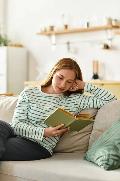 A young woman enjoys her time at home, reading intently on a plush sofa in a cozy atmosphere. — Stock Photo