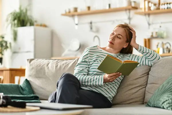 Una mujer joven disfruta leyendo un libro mientras se relaja cómodamente en su acogedor espacio en casa. - foto de stock