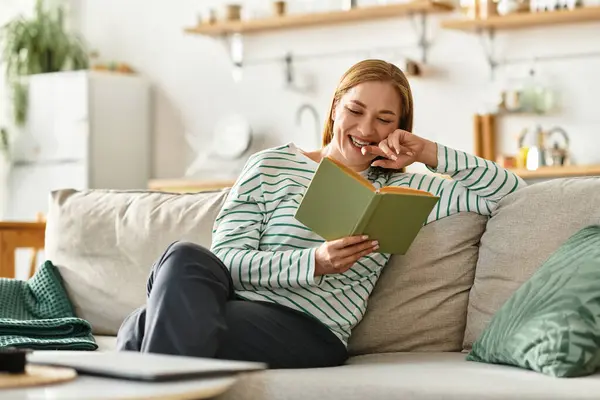 A young woman quietly laughs while reading in her cozy, inviting living space. — Stock Photo