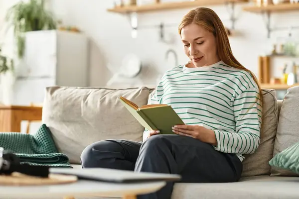 Giovane donna gode di un momento di pace a casa durante la lettura di un libro su un accogliente divano. — Foto stock