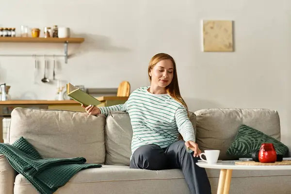 Giovane donna gode di relax a casa con un libro e una bevanda calda in un ambiente accogliente. — Foto stock