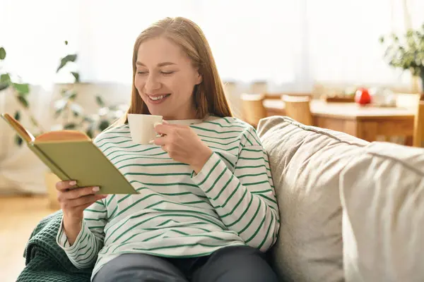 A young woman relaxes at home with a book and tea, basking in the sunlight. — Stock Photo