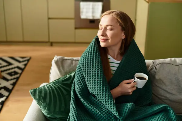 Relaxing in a cozy space, a young woman sips coffee while wrapped in a soft blanket. — Stock Photo