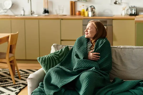 A young woman cherishes a tranquil afternoon at home, wrapped in a cozy blanket, smiling gently. — стоковое фото