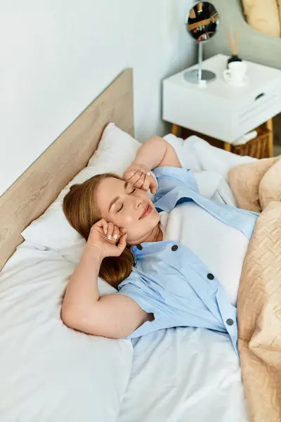 Una joven mujer se estira pacíficamente en la cama, saboreando una mañana relajada en su acogedor entorno hogareño. - foto de stock