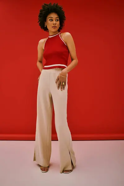 Mujer joven y segura se levanta elegantemente en un atuendo elegante, irradiando moda y belleza en el estudio. - foto de stock
