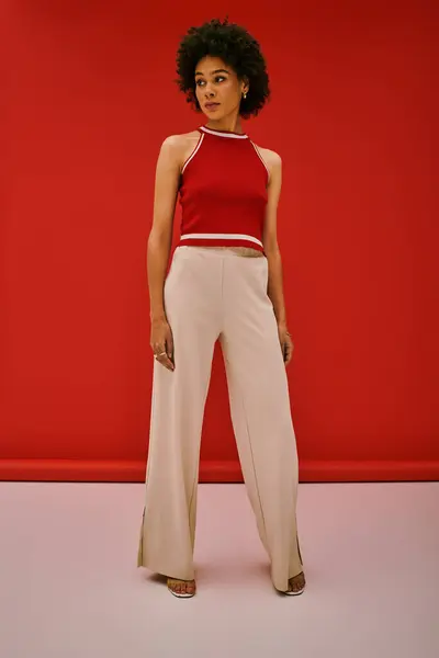 Elegante giovane donna posa con fiducia in abito alla moda contro un vivido sfondo rosso, stile trasudante. — Foto stock