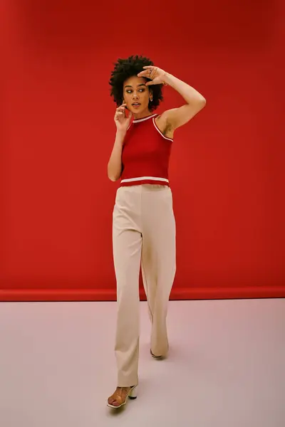 A young woman in stylish attire walks confidently against a bold red backdrop. — Stock Photo