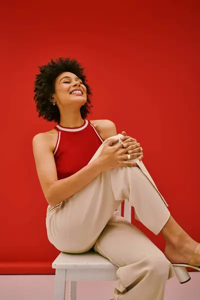 Radiant young woman exudes happiness while posing in trendy attire on a white stool. — Stock Photo