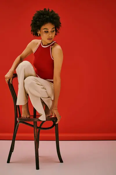 Woman showcases her unique style while perched on a wooden chair in a striking red setting. — Stock Photo