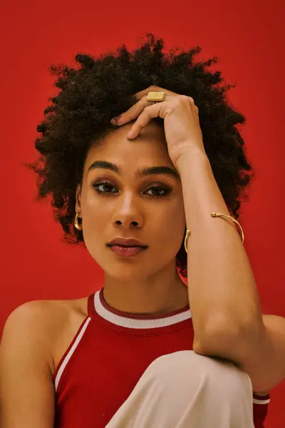 Mujer joven posa elegantemente con una expresión llamativa sobre un fondo rojo audaz. - foto de stock