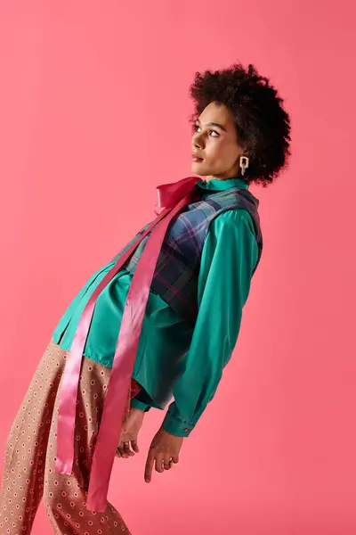 A confident young woman models unique clothing against a pink wall. — Stock Photo