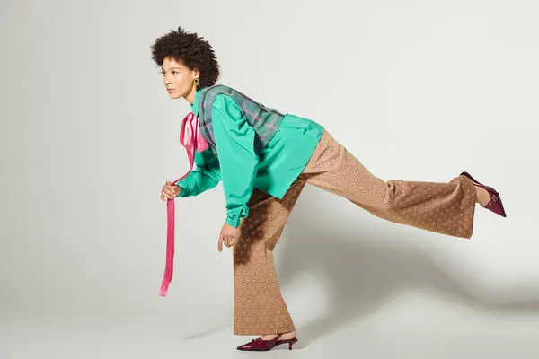 En un entorno de estudio creativo, una mujer joven alcanza una pose dinámica con estilo y moda vibrante. - foto de stock