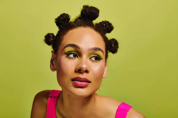 Mujer joven muestra un peinado juguetón, maquillaje de ojos verdes y una parte superior rosa. - foto de stock