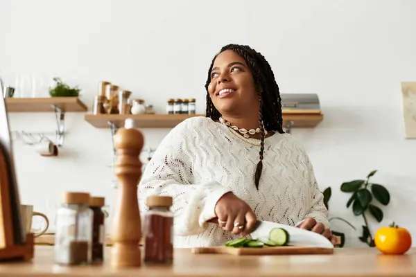 In a bright home kitchen, a young African American woman cuts vegetables with a smile. — Stock Photo