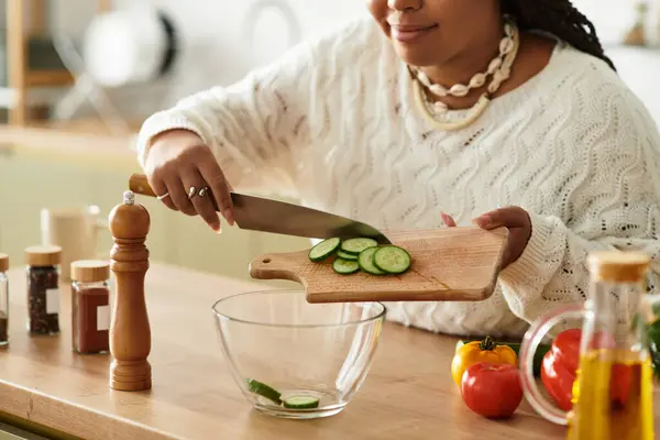 Jovem afro-americana prepara alegremente uma salada saudável enquanto sorri em sua cozinha. — Fotografia de Stock