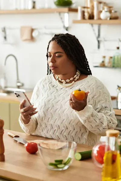 Jovem afro-americana se envolve na preparação de uma salada colorida enquanto usa seu telefone. — Fotografia de Stock