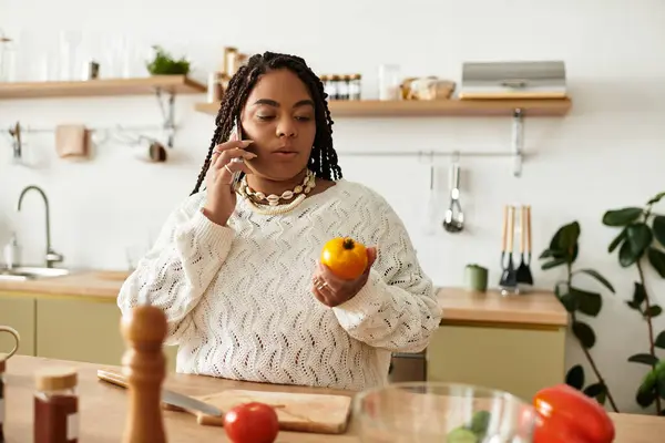 Uma jovem negra cozinha uma salada em casa, concentrando-se em ingredientes durante uma chamada. — Fotografia de Stock