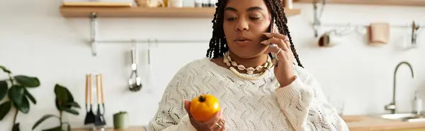 Young african american woman prepares a vibrant salad while chatting on the phone in her kitchen, banner — Stock Photo