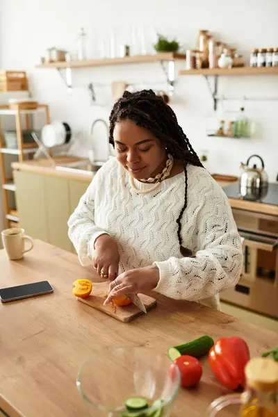 A young Black woman chops fresh veggies in her cozy kitchen, happily enjoying cooking. — Stock Photo